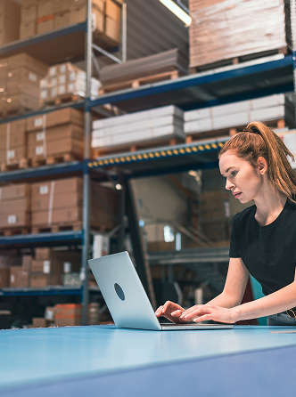 A woman working on her laptop inside a warehouse office, managing support and services for a trusted traffic signs supplier Perth