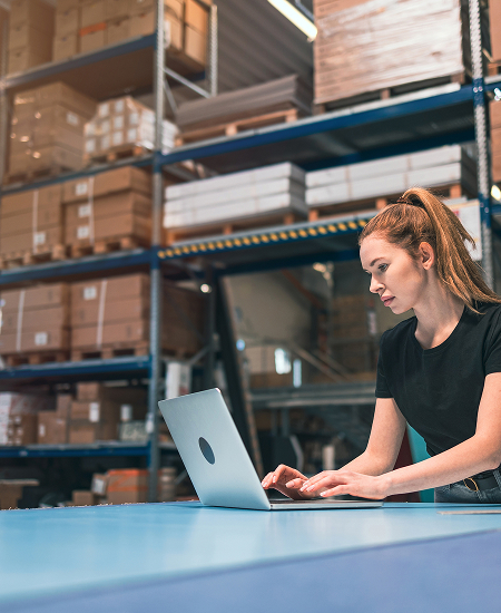 A woman working on her laptop inside a warehouse office, managing support and services for a trusted traffic signs supplier Perth